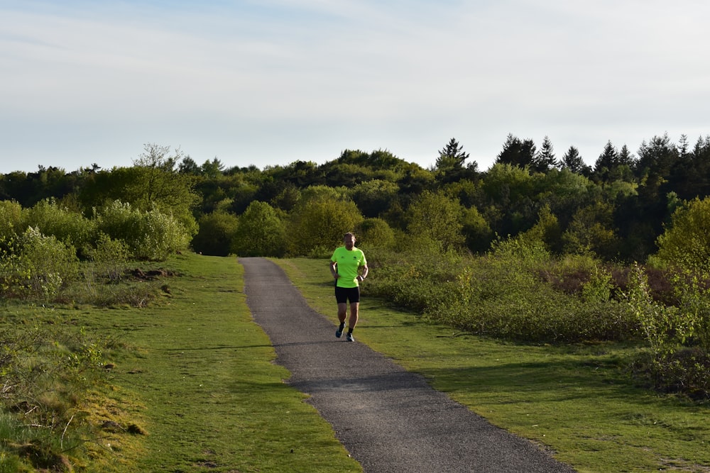 man in green shirt walking on pathway between green grass field during daytime