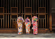 2 women in kimono standing on sidewalk during daytime