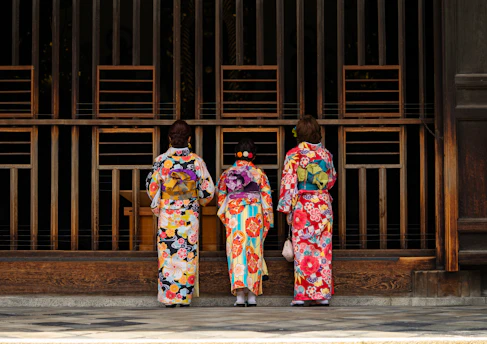 2 women in kimono standing on sidewalk during daytime