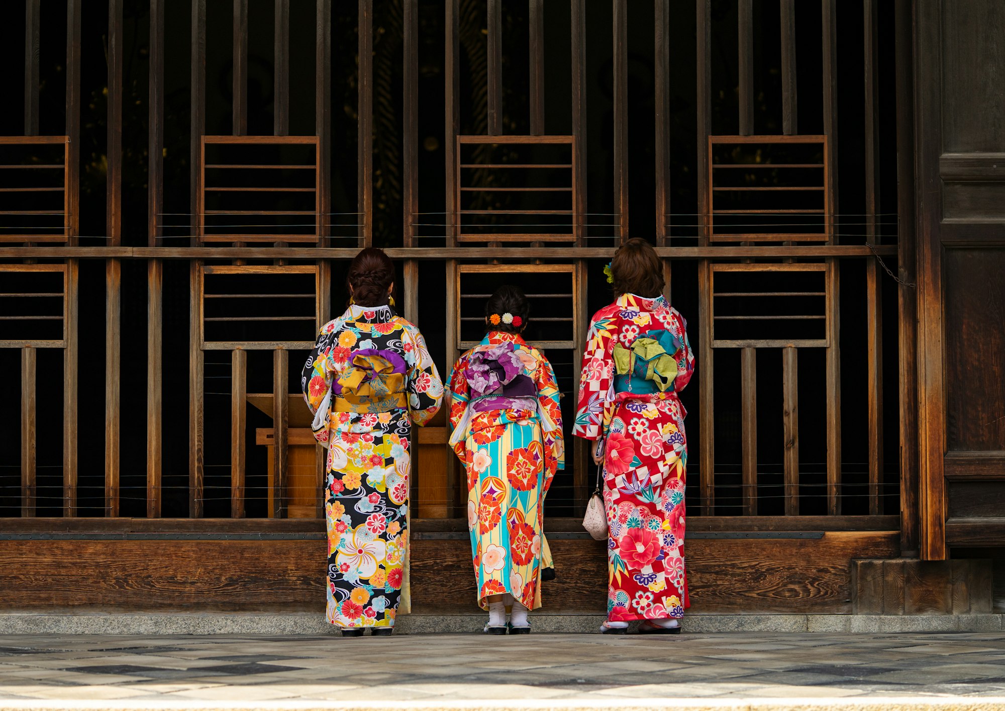 Traditional temple in Kyoto (Japan) with three women in front of a wooden gate. Wearing beautiful, colourful dresses on a sunny day in spring.