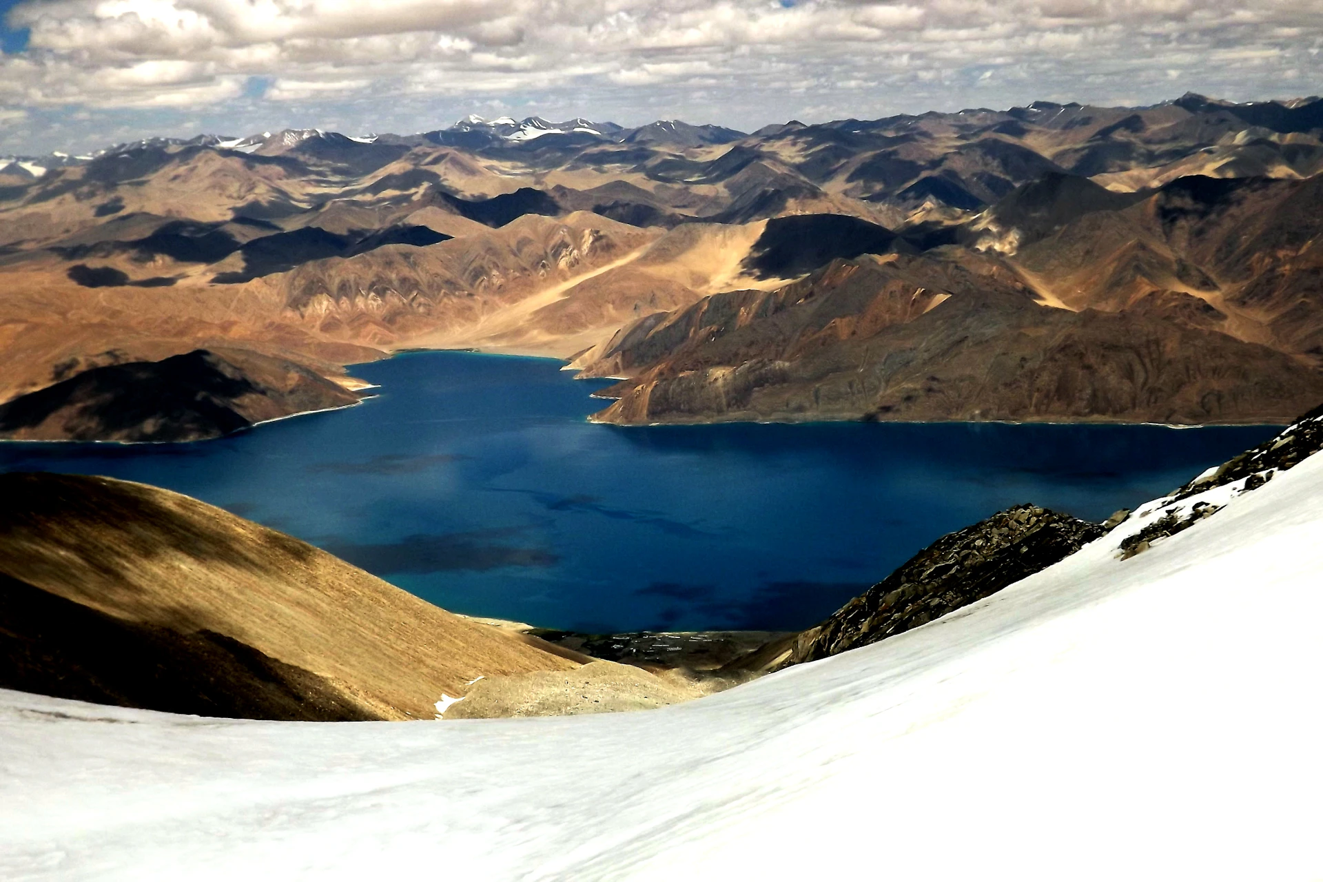 Crystal-clear blue waters of Laguna Humantay reflecting the surrounding snowy peaks under a bright sky.