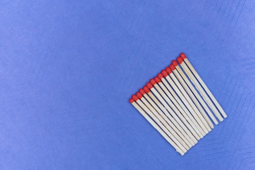 A group of wooden matchsticks with red tips arranged in parallel on a textured blue surface.