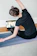 A smiling woman in her 30s doing a gentle seated neck stretch at her office desk.