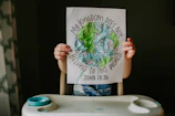 A joyful child holding up a completed coloring activity featuring a Bible verse