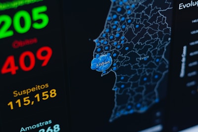 Detailed map displaying data visualization with blue circular markers representing specific data points across a geographical area labeled with city names such as Lisbon and Evora. Bold, brightly colored numerical statistics appear on the left side with the terms 'Suspeitos' and 'Amostras,' suggesting a context of data tracking or analysis.