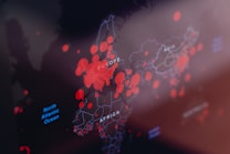A digital map highlights various regions with differently sized red circles, indicating concentration or intensity of certain data points, overlaid on continents such as Europe, Africa, and part of Asia. Labels in white define geographical markers including oceans and continents with faint outlines in the background.