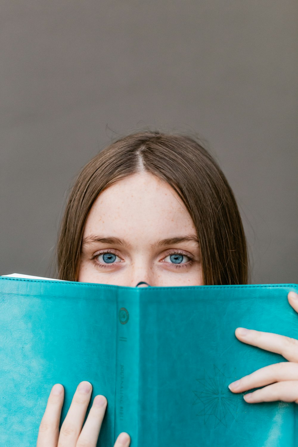 woman covering her face with teal book