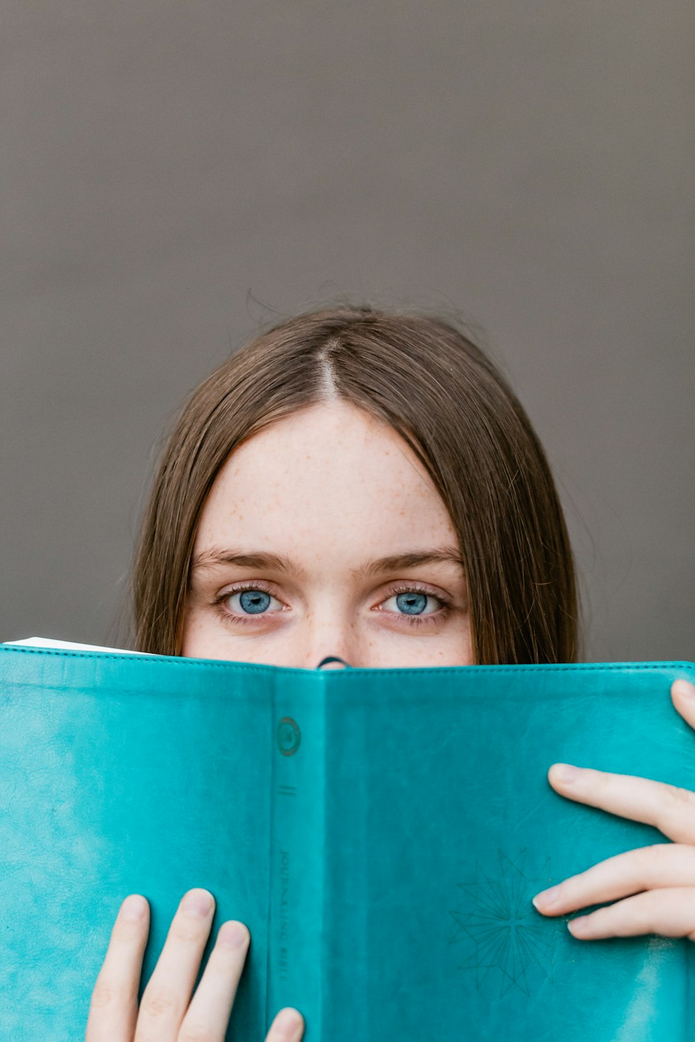 donna che si copre il viso con il libro verde acqua