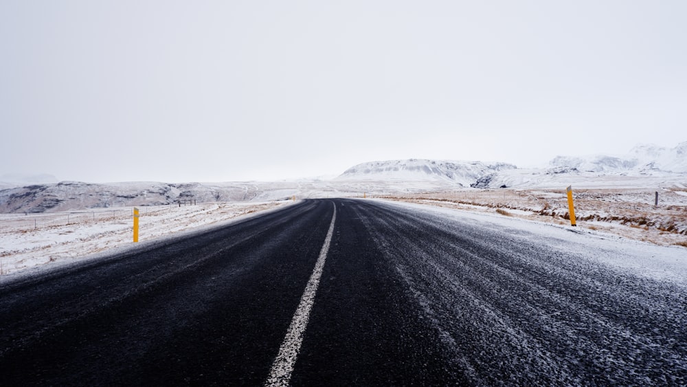 black asphalt road in the middle of white snow covered field during daytime