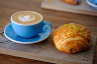 Close-up of a Cafecup cup with a creative sleeve design, placed next to a croissant on a rustic table.