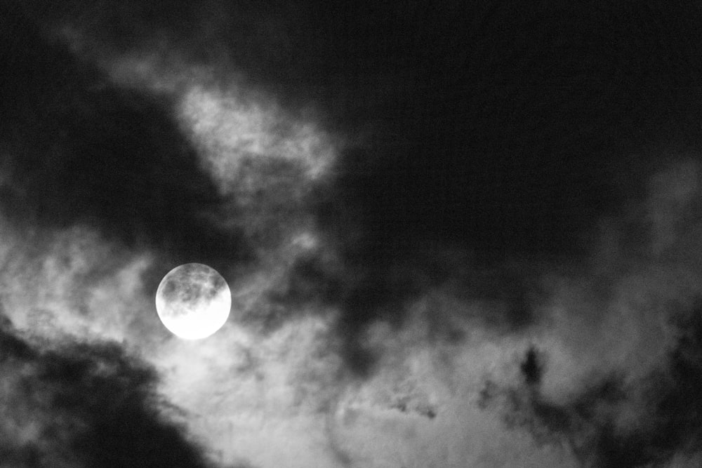 grayscale photo of moon in dark clouds