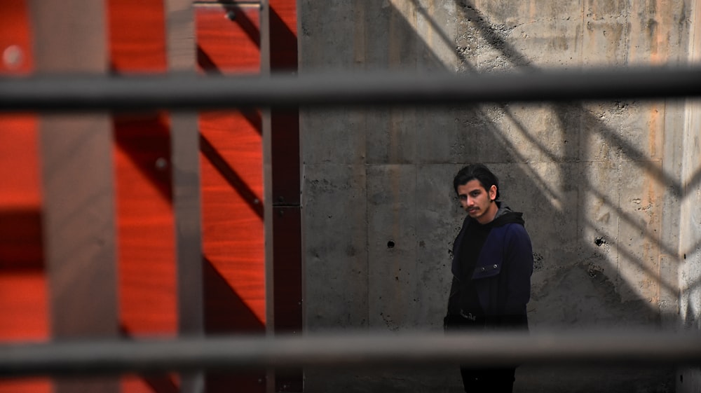 man in black jacket standing beside red metal gate