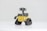 A small robot with large binocular-style eyes, tank-like treads, and a yellow cubical body, standing on a plain white surface. The robot has a distinctively cute and curious appearance.