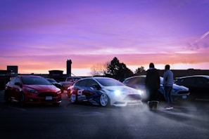 A group of car lovers socializing beside a variety of sports cars at sunset