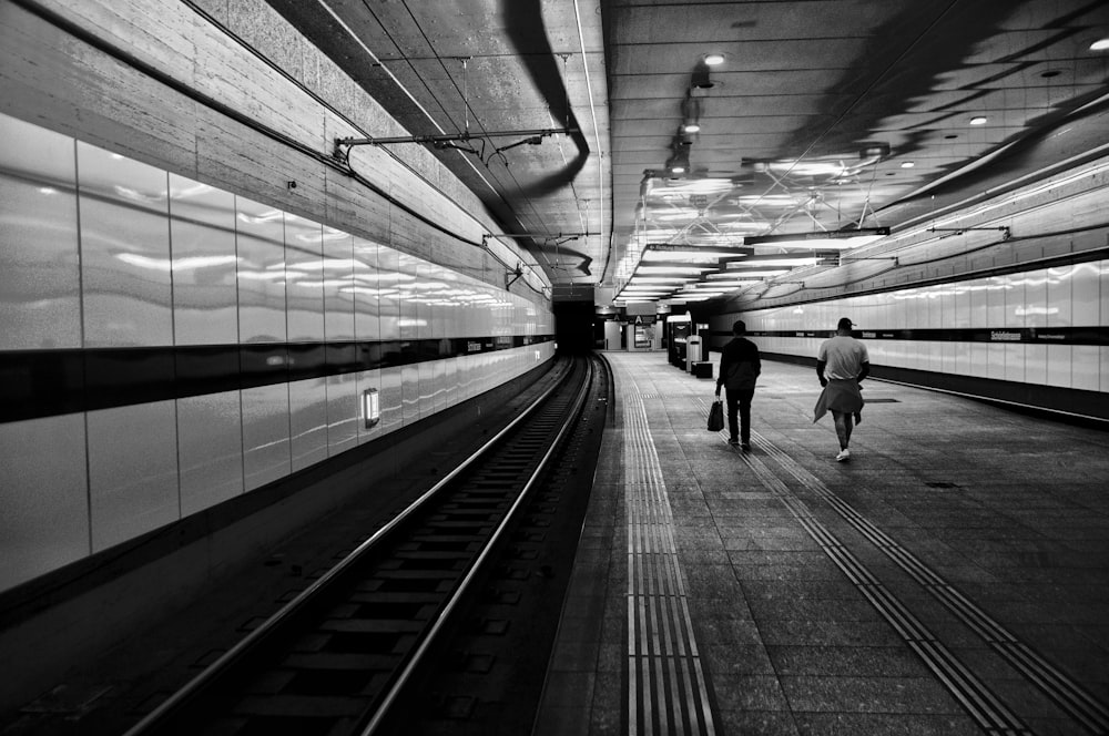 grayscale photo of man walking on train station