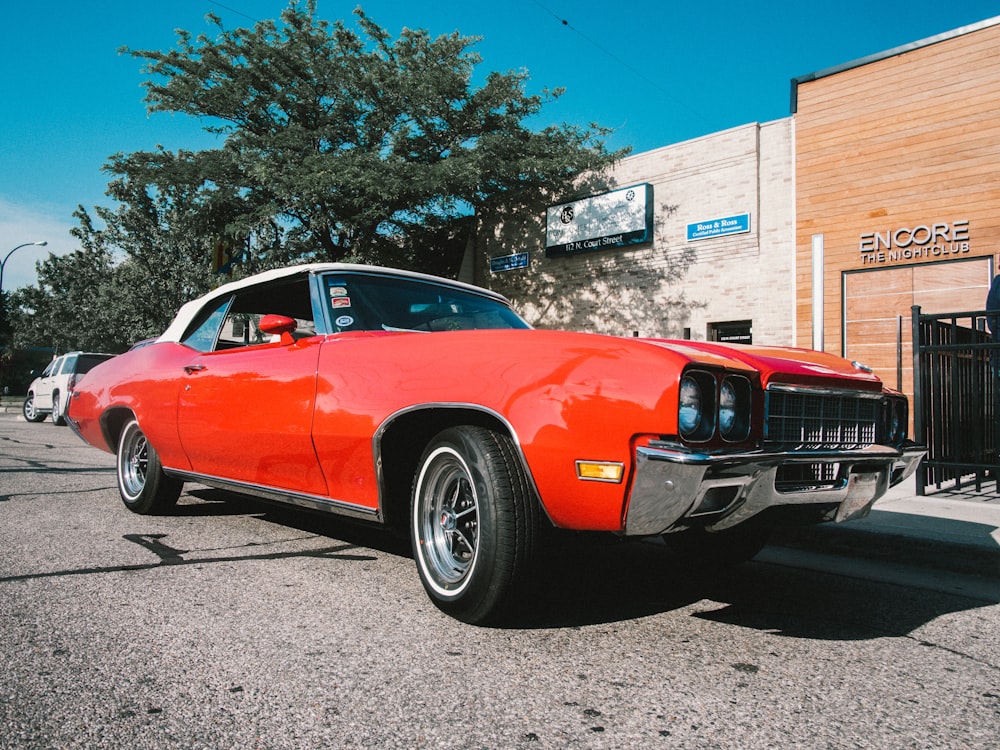 muscle car arancione parcheggiata vicino a un edificio in cemento marrone durante il giorno