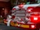 The front of a fire truck is prominently featured, showcasing its bright red color and shiny chrome details. Numerous lights are illuminated, casting a glowing and attention-grabbing effect. Coiled fire hoses and equipment are securely fastened to the truck's bumper, with the number 421 clearly visible.