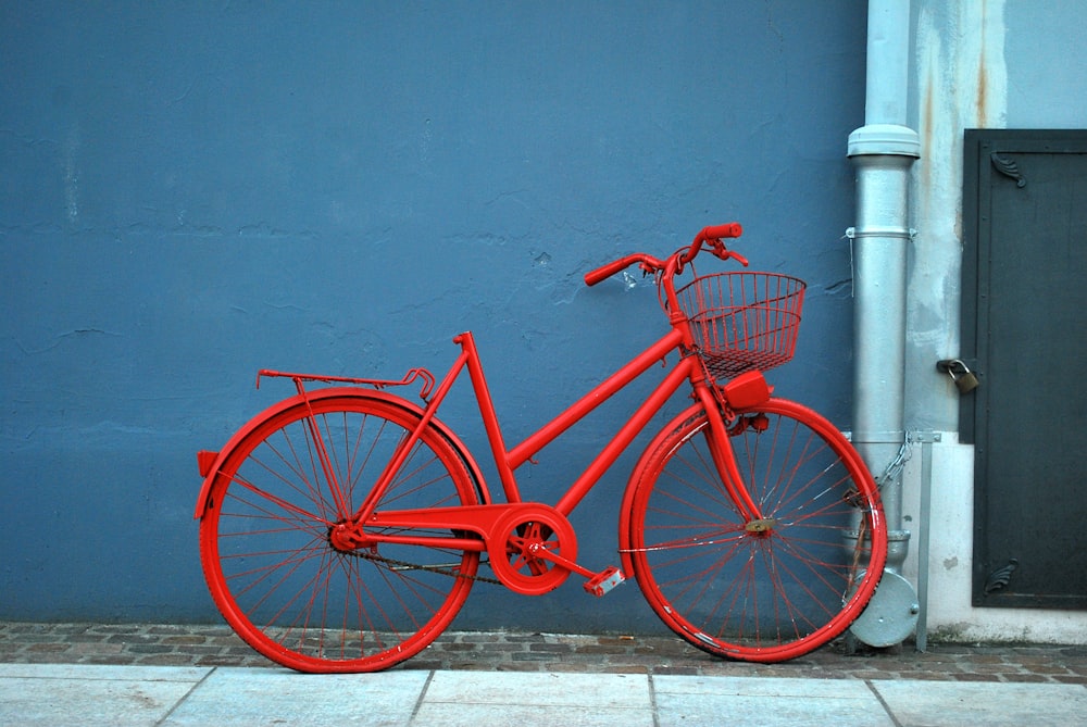 red city bike parked beside blue painted wall