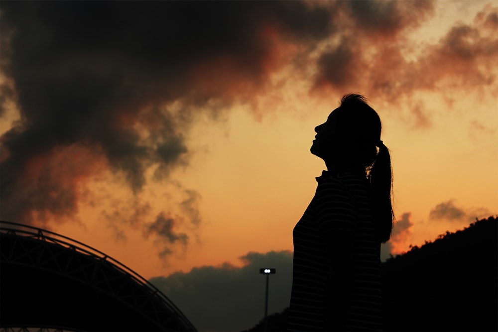 silhouette of woman standing under orange sky during sunset