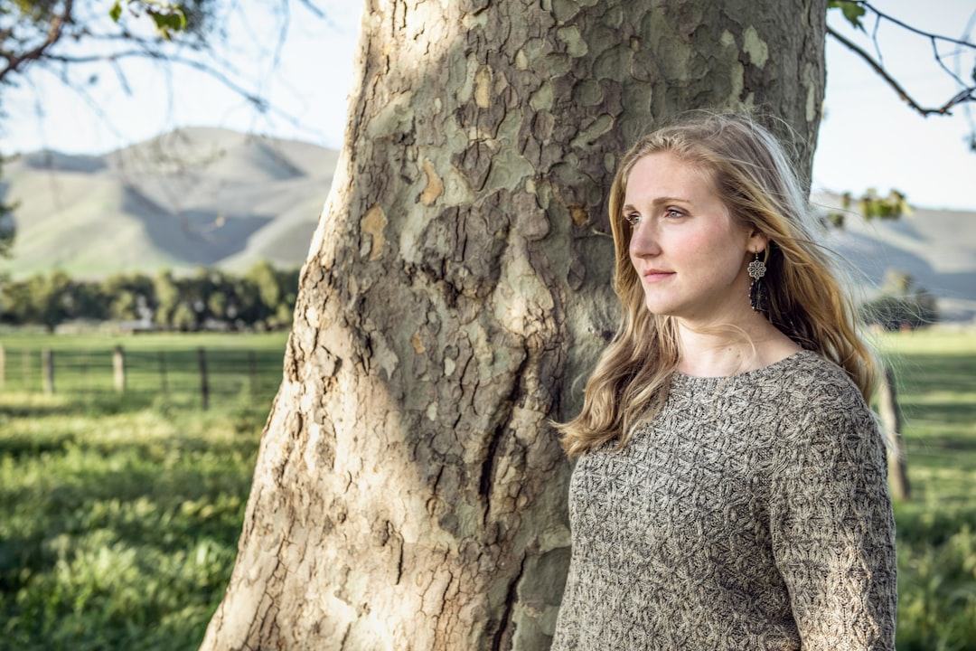 woman in gray v neck shirt standing beside brown tree during daytime