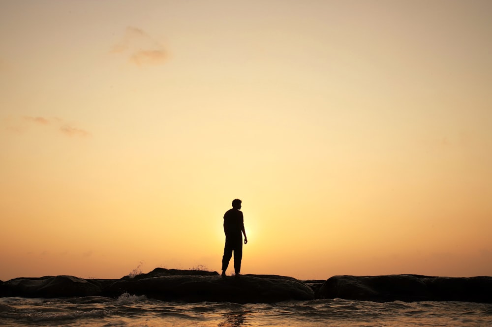 silhouette of man standing on seashore during sunset