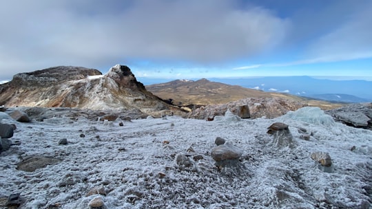 rocky river with snow covered ground and mountains in distance under white clouds and blue sky in Parque Nacional Natural Los Nevados Colombia