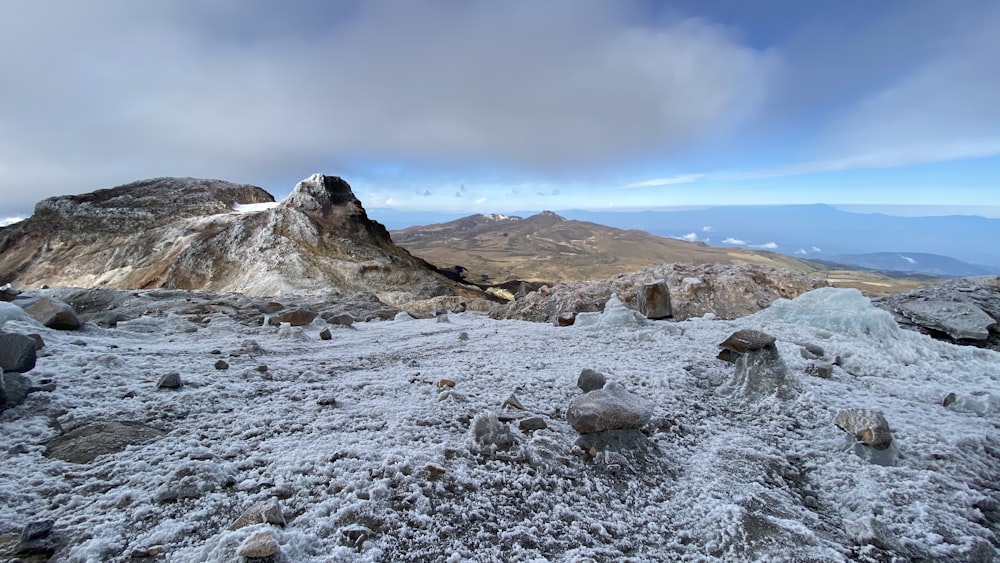 rocky river with snow covered ground and mountains in distance under white clouds and blue sky