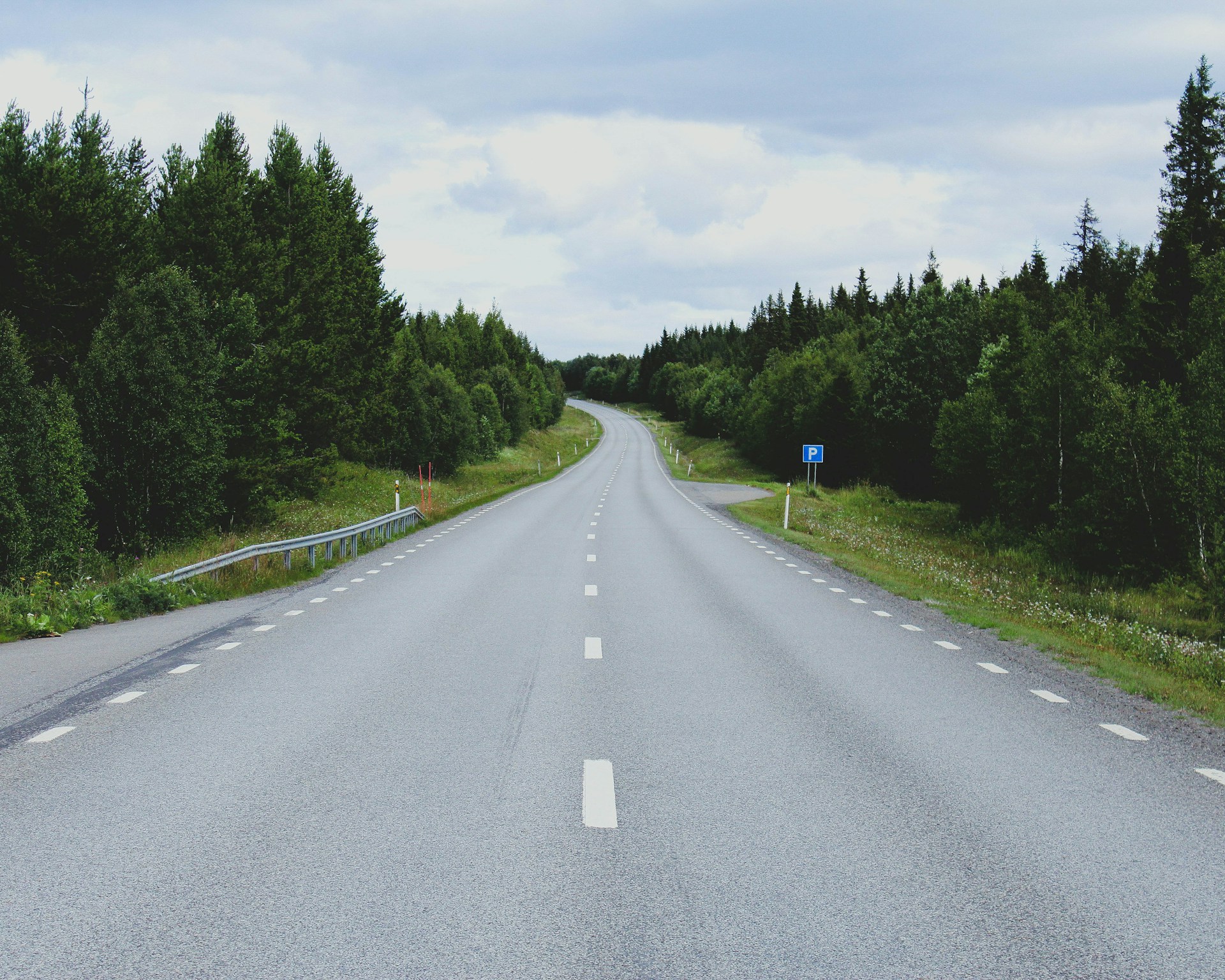 gray concrete road between green trees under white clouds during daytime
