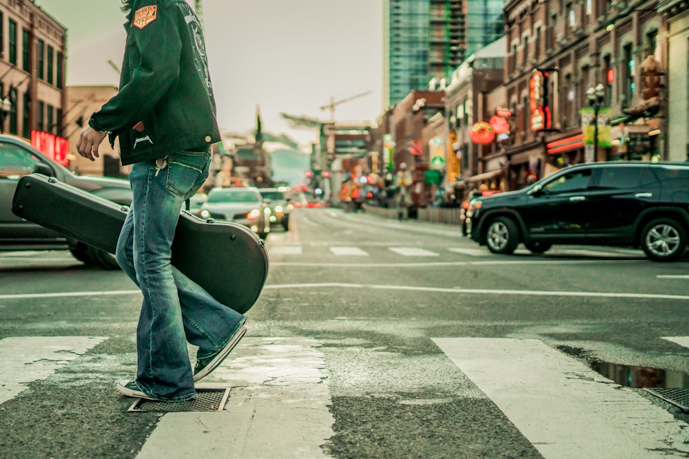 man in green jacket and blue denim jeans walking on sidewalk during daytime