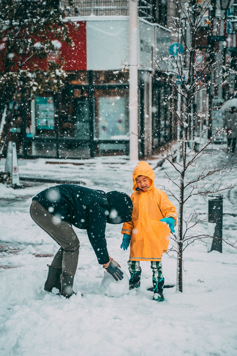 Kind in gelber Jacke und schwarzer Hose, das tagsüber auf schneebedecktem Boden spielt