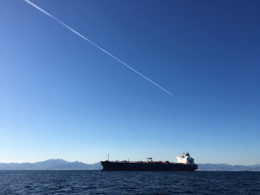 A majestic cargo ship cutting through deep navy blue ocean waters under a clear sky, with a faint global map overlay.