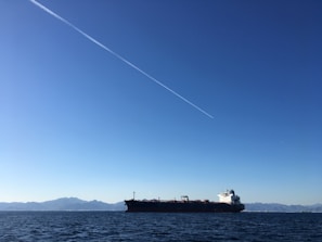 A large cargo ship loaded with containers sailing under a clear blue sky.