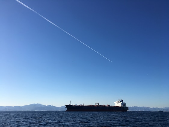 A modern cargo ship cutting through deep blue ocean waters under a clear sky.