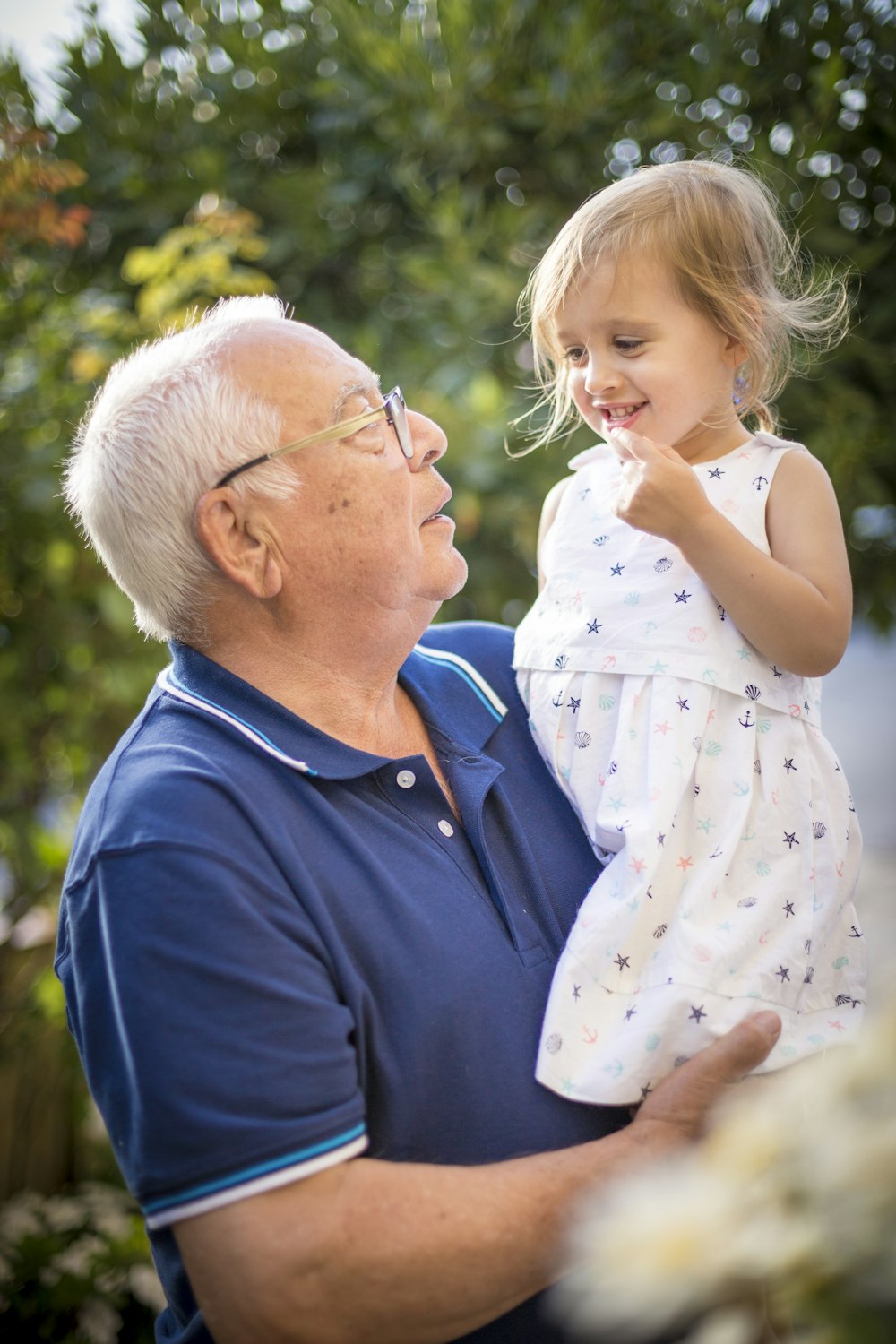 man in blue polo shirt carrying girl in white and pink floral dress