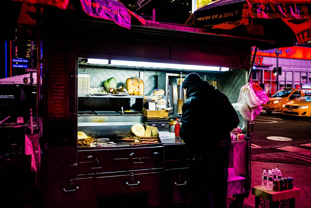 man in black jacket standing in front of food stall