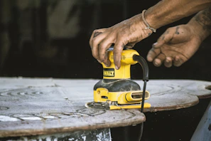 Artisan sanding a wooden table surface outdoors with natural light