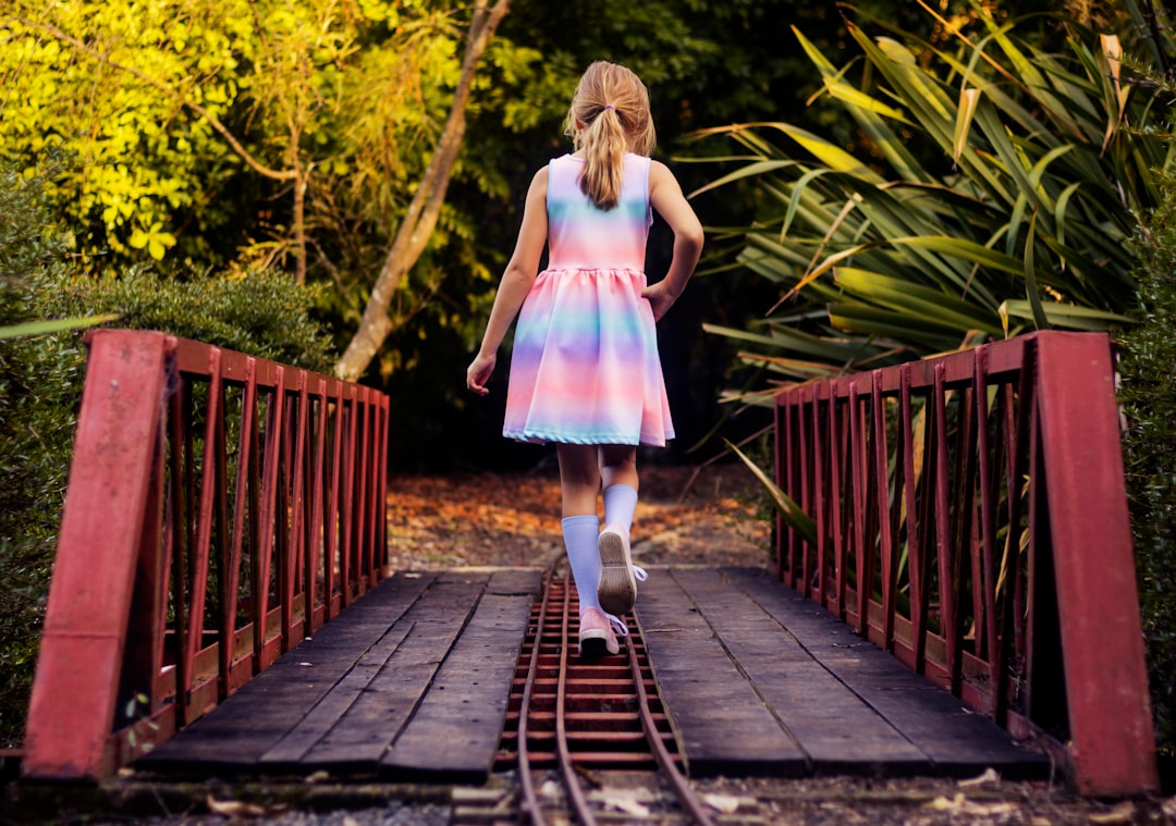 girl in pink dress walking on wooden bridge