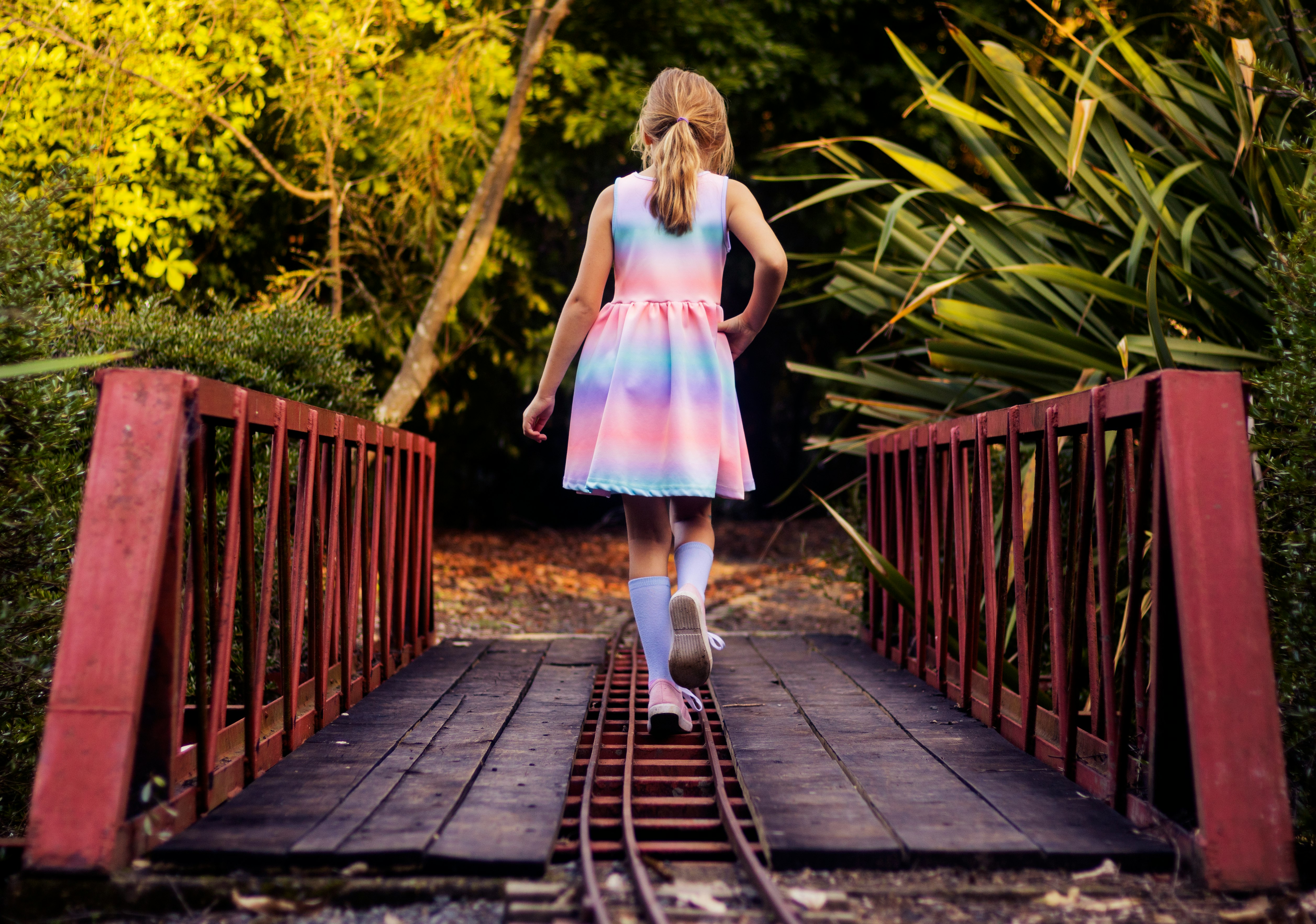 girl in pink dress walking on wooden bridge