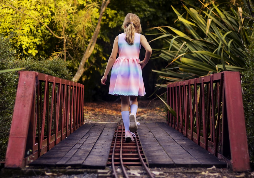 girl in pink dress walking on wooden bridge