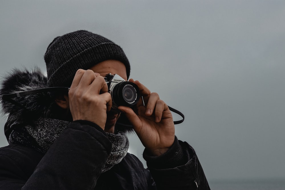 person in black knit cap holding black dslr camera