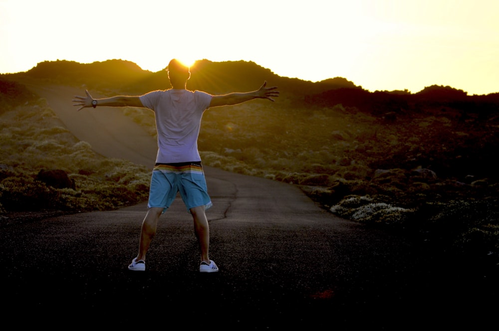 man in white shirt and blue shorts standing on gray sand during daytime