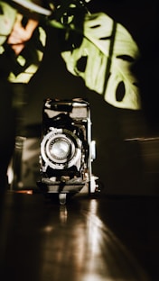 A moody, artistic shot of a vintage camera resting on a terracotta brown surface with aqua blue light casting shadows.