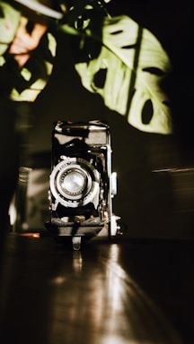 A moody, artistic shot of a vintage camera resting on a terracotta brown surface with aqua blue light casting shadows.