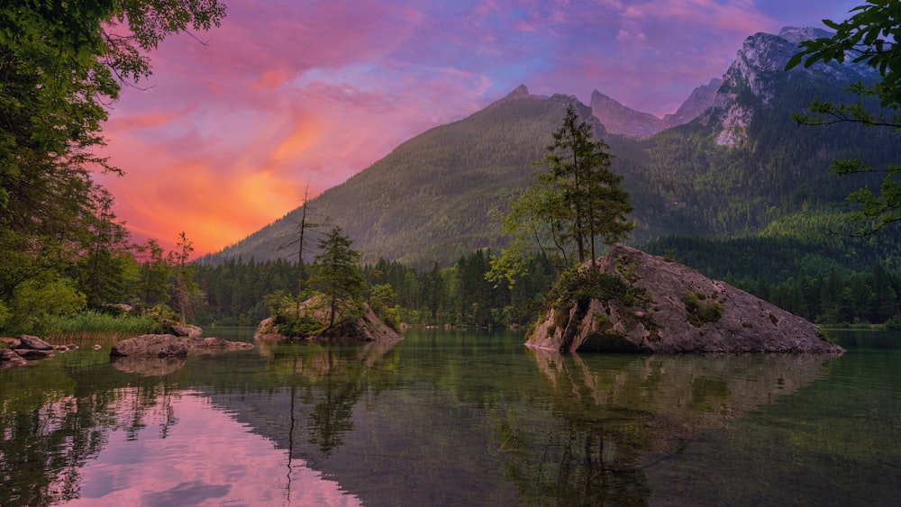 green trees near lake and mountain during sunset