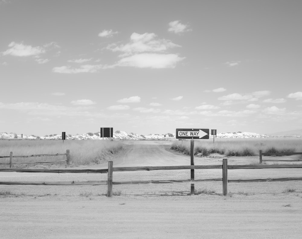 Foto en escala de grises de una valla de madera con una distancia en un campo cubierto de nieve
