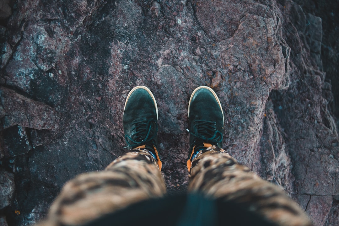 person in black and white sneakers standing on brown rock
