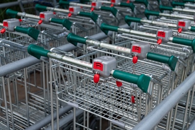 A collection of metal shopping carts with green and red handles are lined up in rows. Each cart includes a lock mechanism with a chain attached to the handle.
