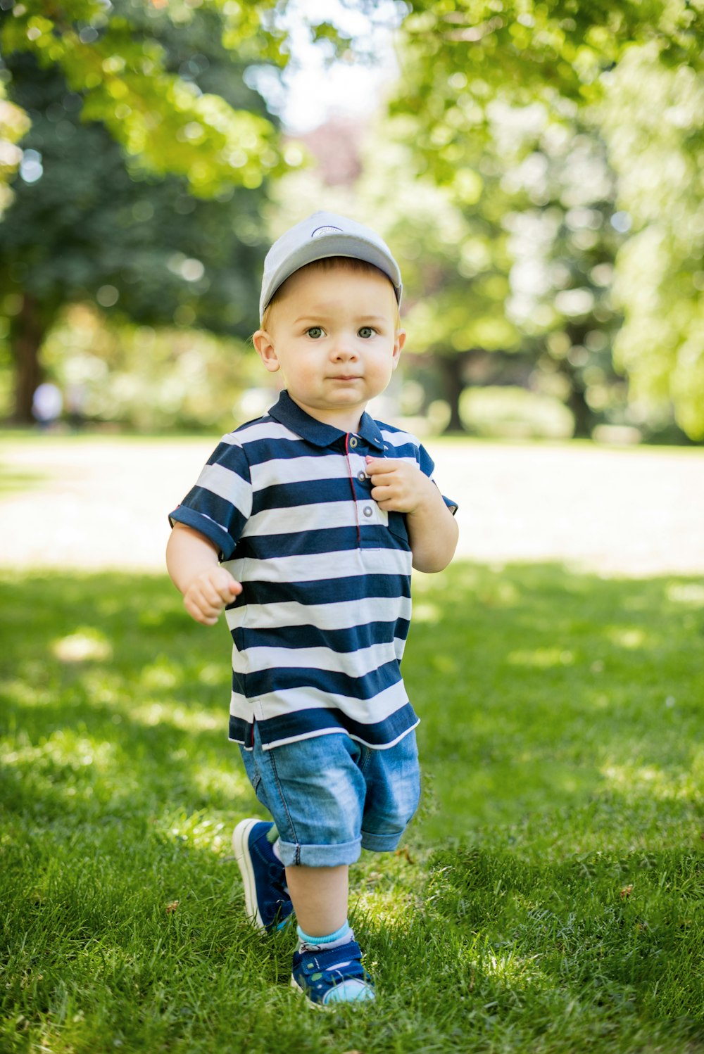 child in blue and white striped shirt and blue denim jeans standing on green grass field