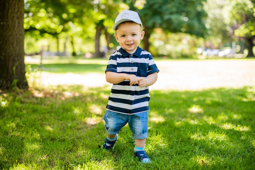 boy in black and white stripe polo shirt and blue denim shorts standing on green grass