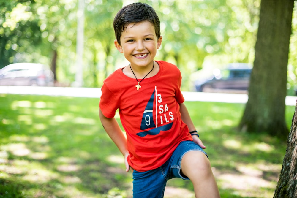 boy in red crew neck t-shirt and blue denim shorts sitting on brown wooden bench